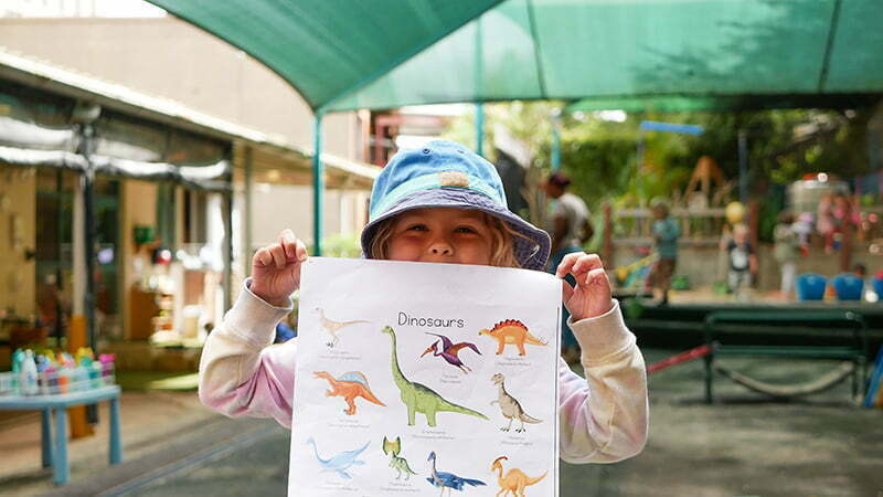 A young boy showing off his coloured illustrations of dinosaurs