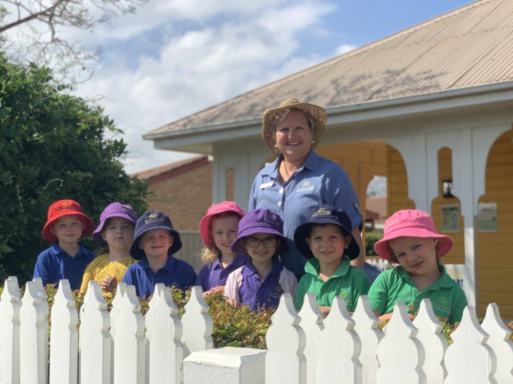 A brightly dressed group of students from a Newcastle Anglican Early Learning Centre line up with an educator outside in their hats, ready for play. 