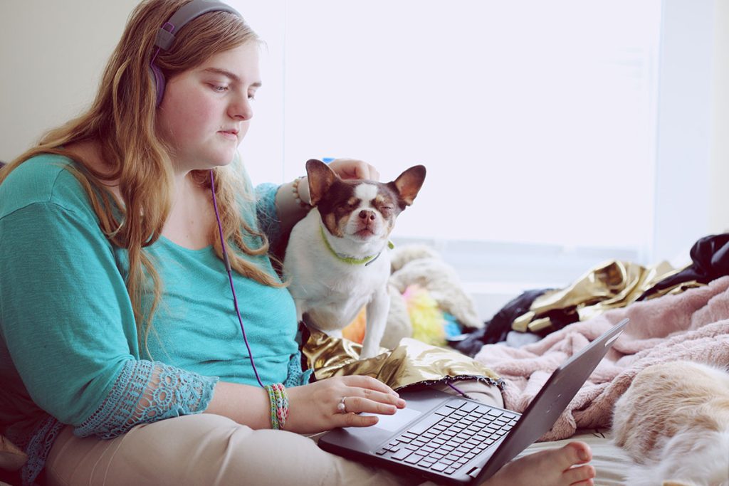A woman with headphones and a laptop on her lap with a dog beside her