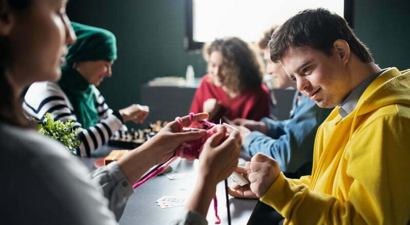 Two female carers teaching teenagers how to play chess and knitting