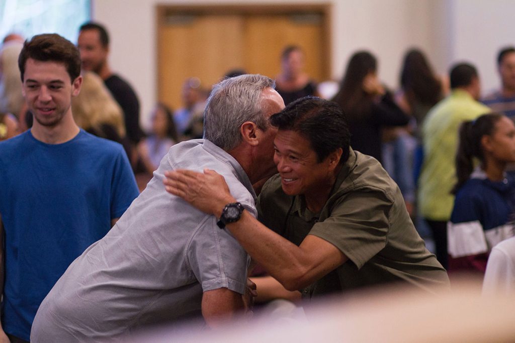 Two males greet and hug each other while other church members are congregating